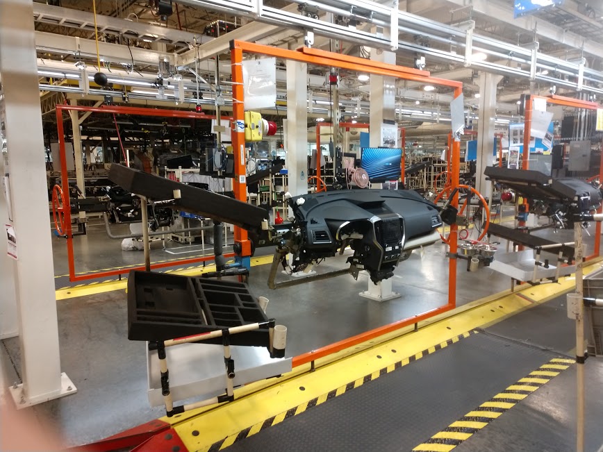 Automobile factory assembly line with car dashboards mounted on orange frames and tools nearby