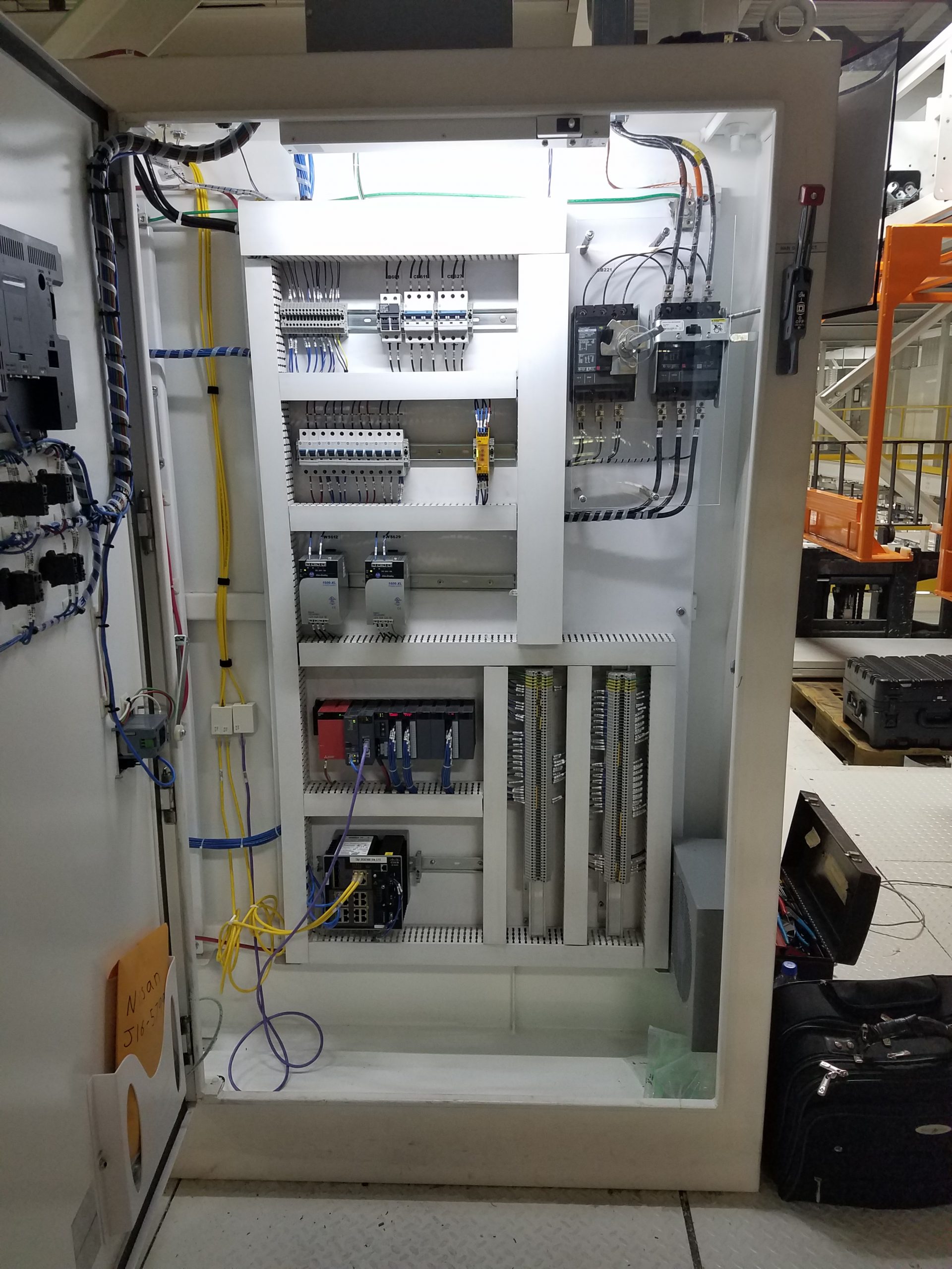 Electrical control panel cabinet with circuit breakers, relays, wiring, a suitcase, and an open toolbox nearby.