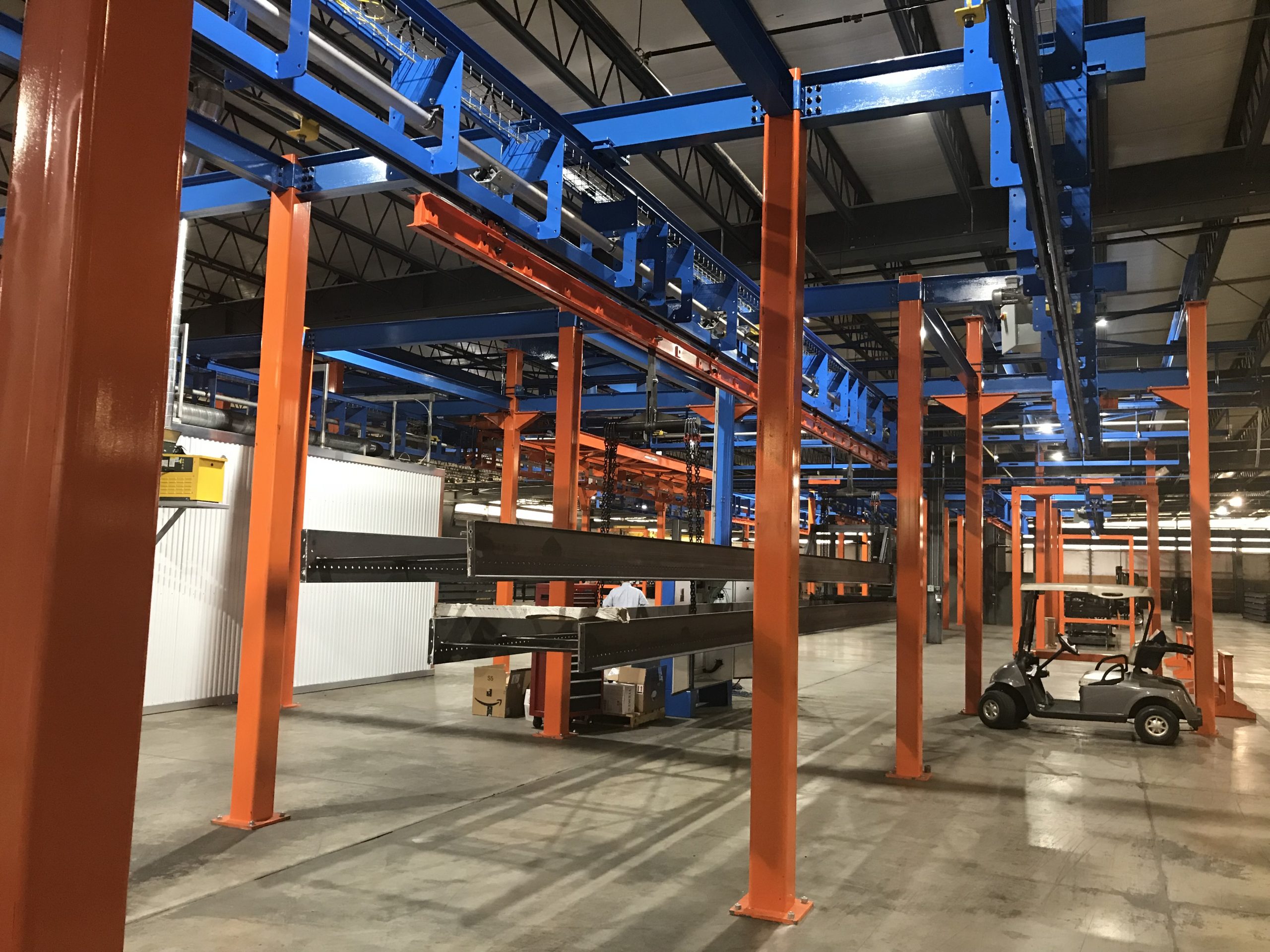 Industrial warehouse with orange and blue overhead metal structures and a parked utility vehicle.