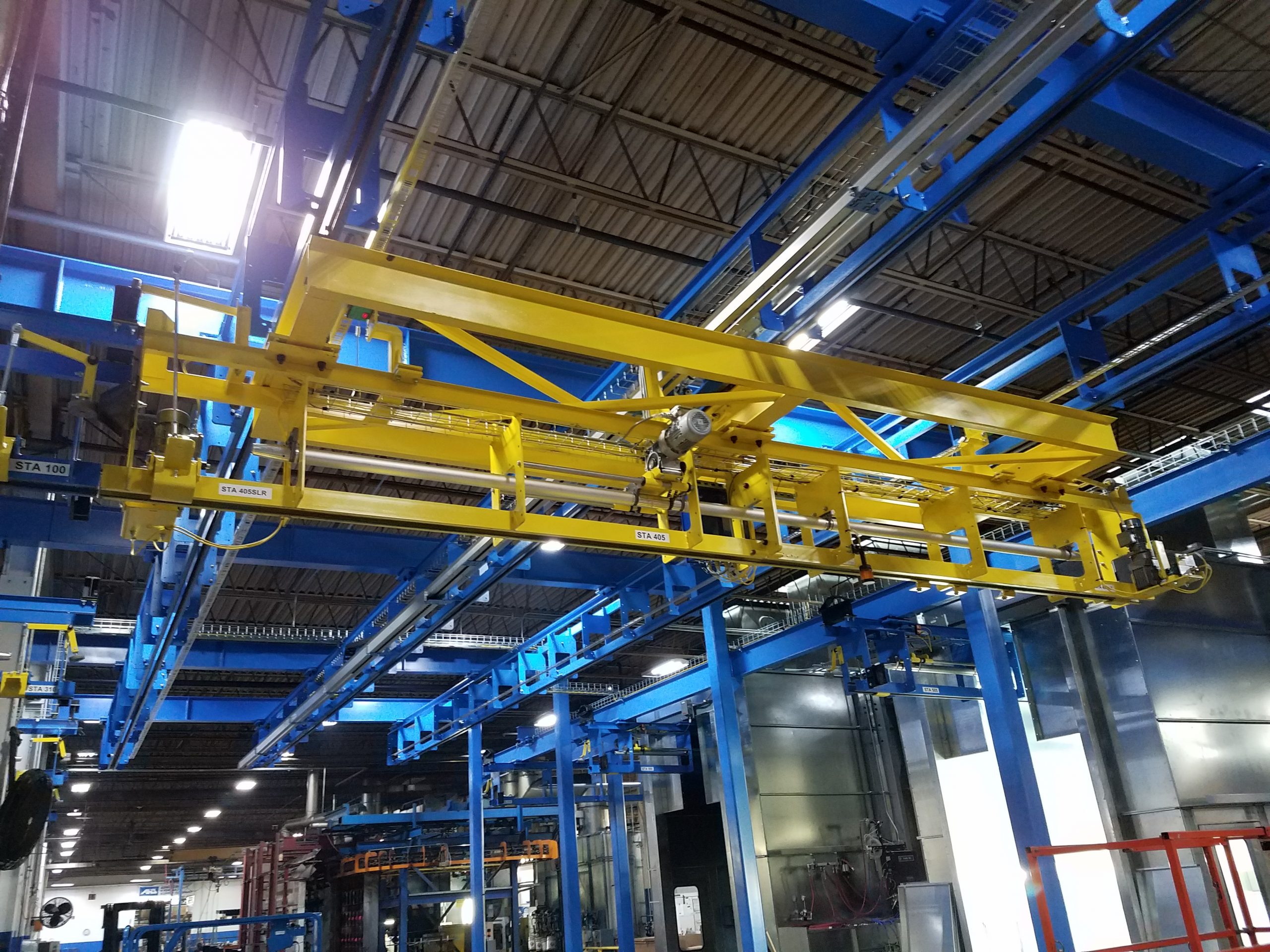 Overhead yellow conveyor system with blue support beams inside an industrial facility.
